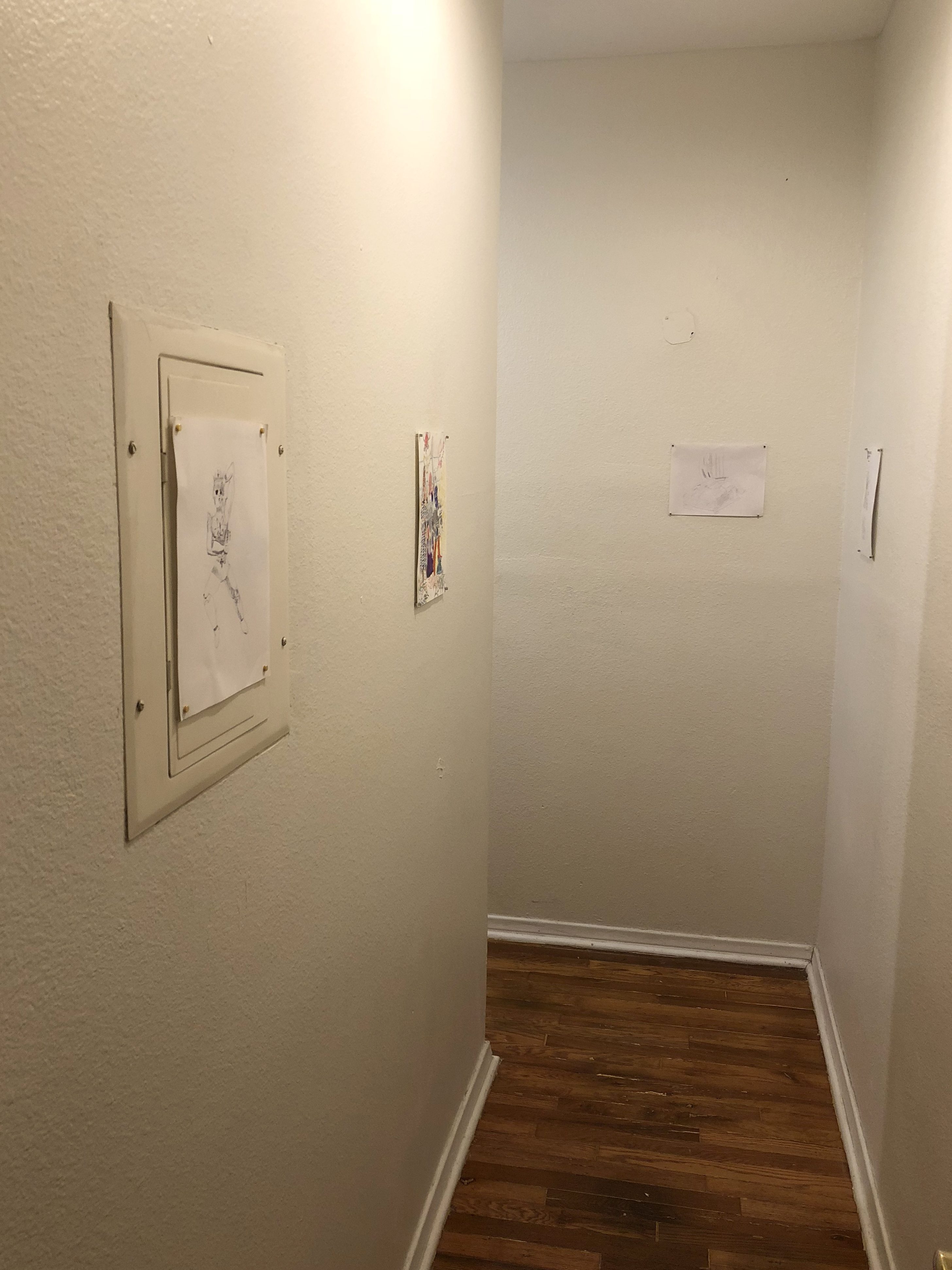 Four drawings on paper hung in a narrow white hallway